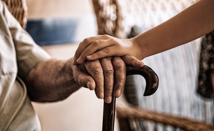 Image: Adobe. Two hands clasped over a walking stick